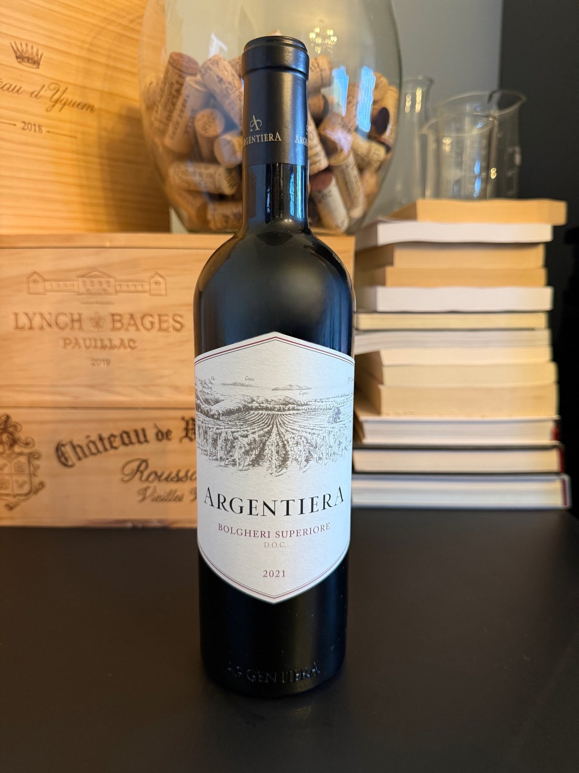 Wine bottle Argentiera Bolgheri Superiore 2021 with books and wooden box in the background.