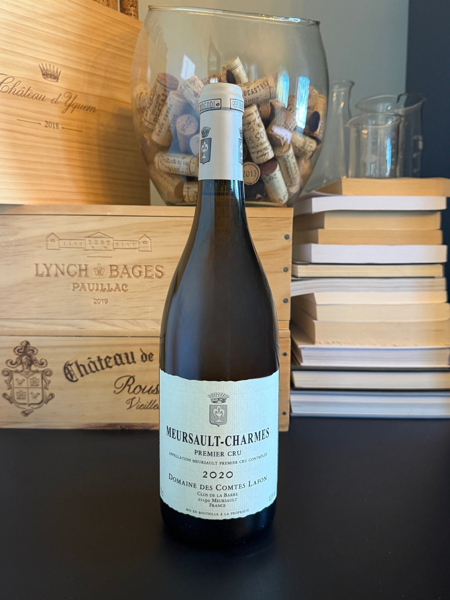 Wine bottle of Domaine des Comtes-Lafon Meursault-Charmes Premier Cru 2020 with a wooden box and cork display in the background