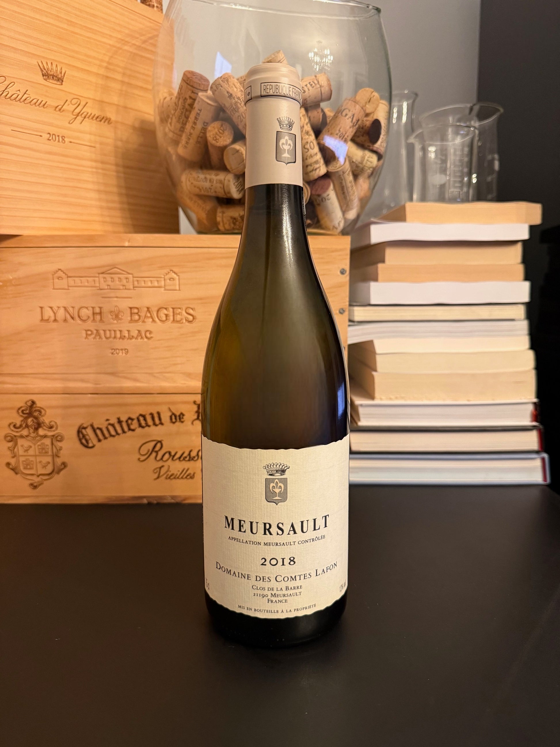 Bottle of Domaine des Comtes Lafon Meursault 2018 wine with a wooden box and books in the background.