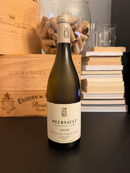 Bottle of Domaine des Comtes Lafon Meursault 2018 wine with a wooden box and books in the background.