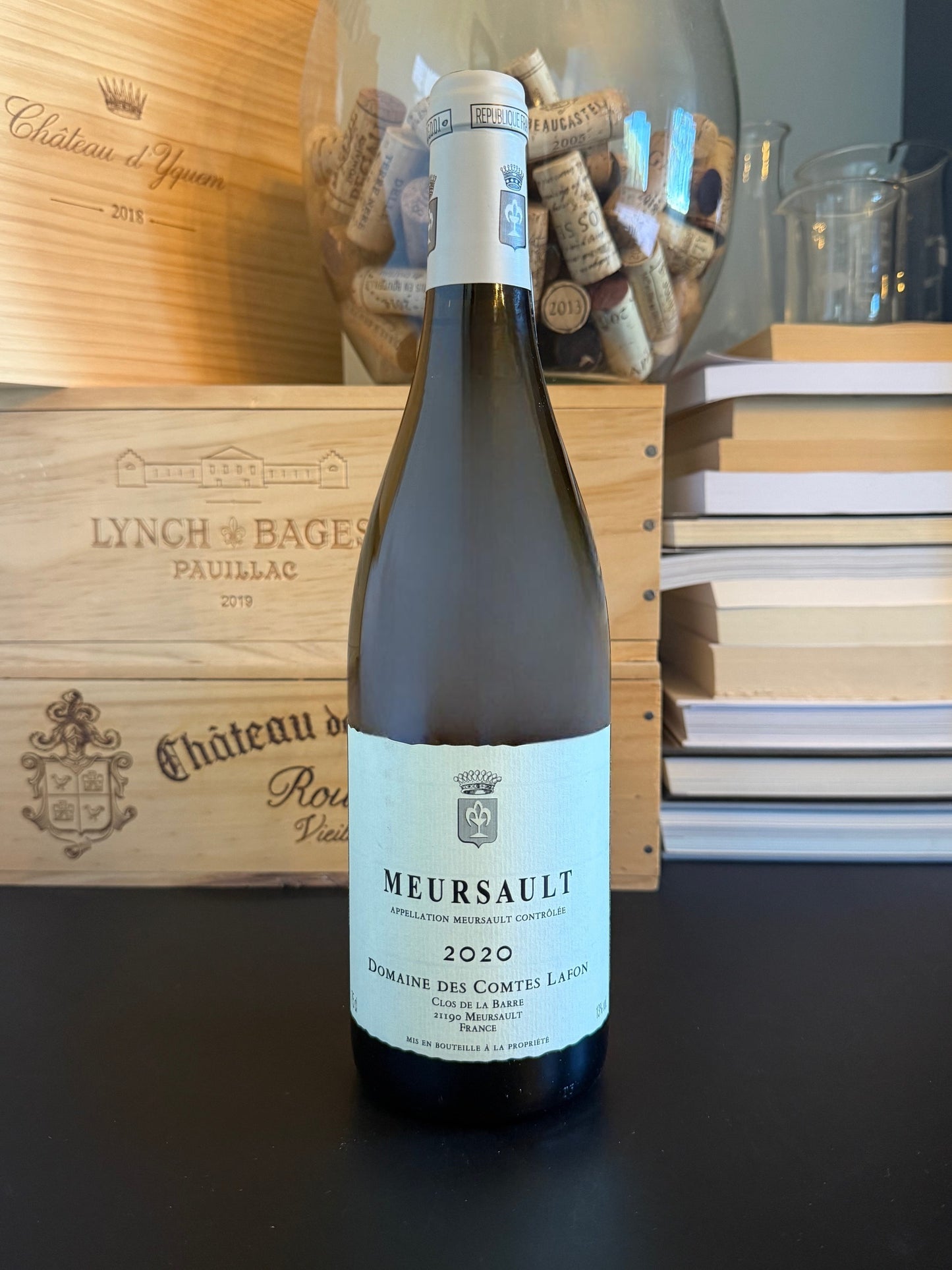 Wine bottle of Domaine des Comtes Lafon Meursault 2020 with a wooden box and books in the background.