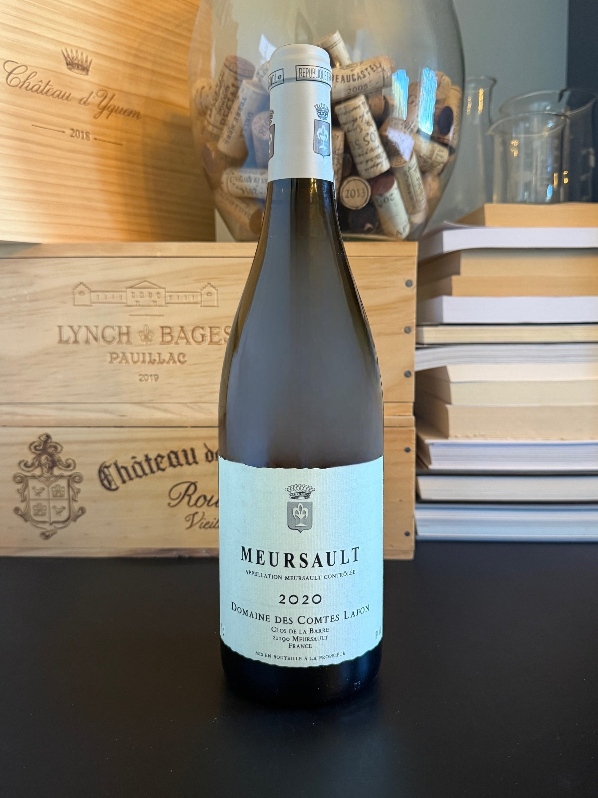 Wine bottle of Domaine des Comtes Lafon Meursault 2020 with a wooden box and books in the background.