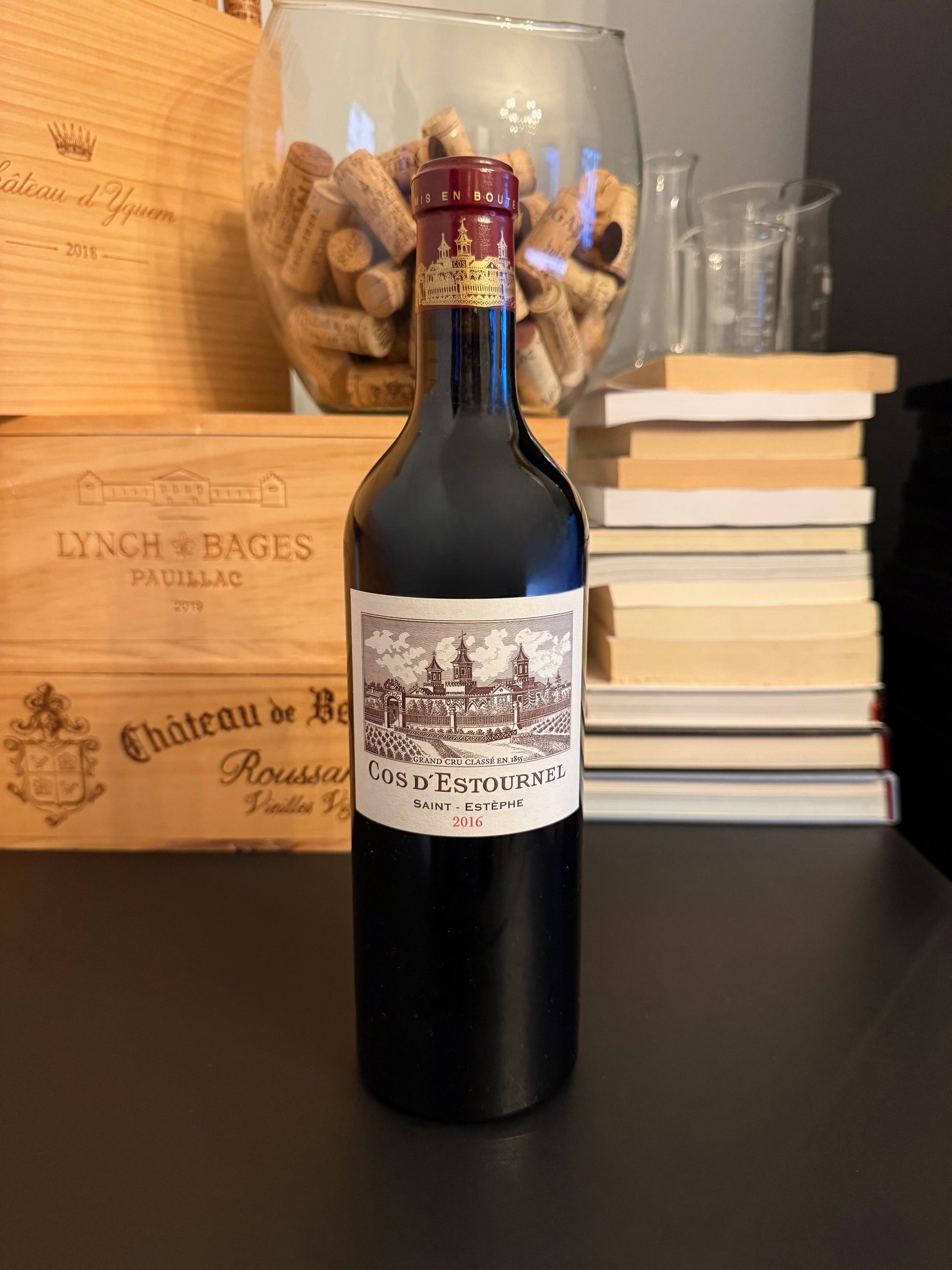 Bottle of Chateau Cos d'Estournel 2016 wine with wooden boxes and books in the background.