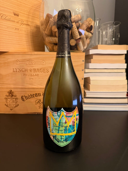 Bottle of Dom Pérignon Vintage 2015: Basquiat Special Edition with a wooden box and books in the background.