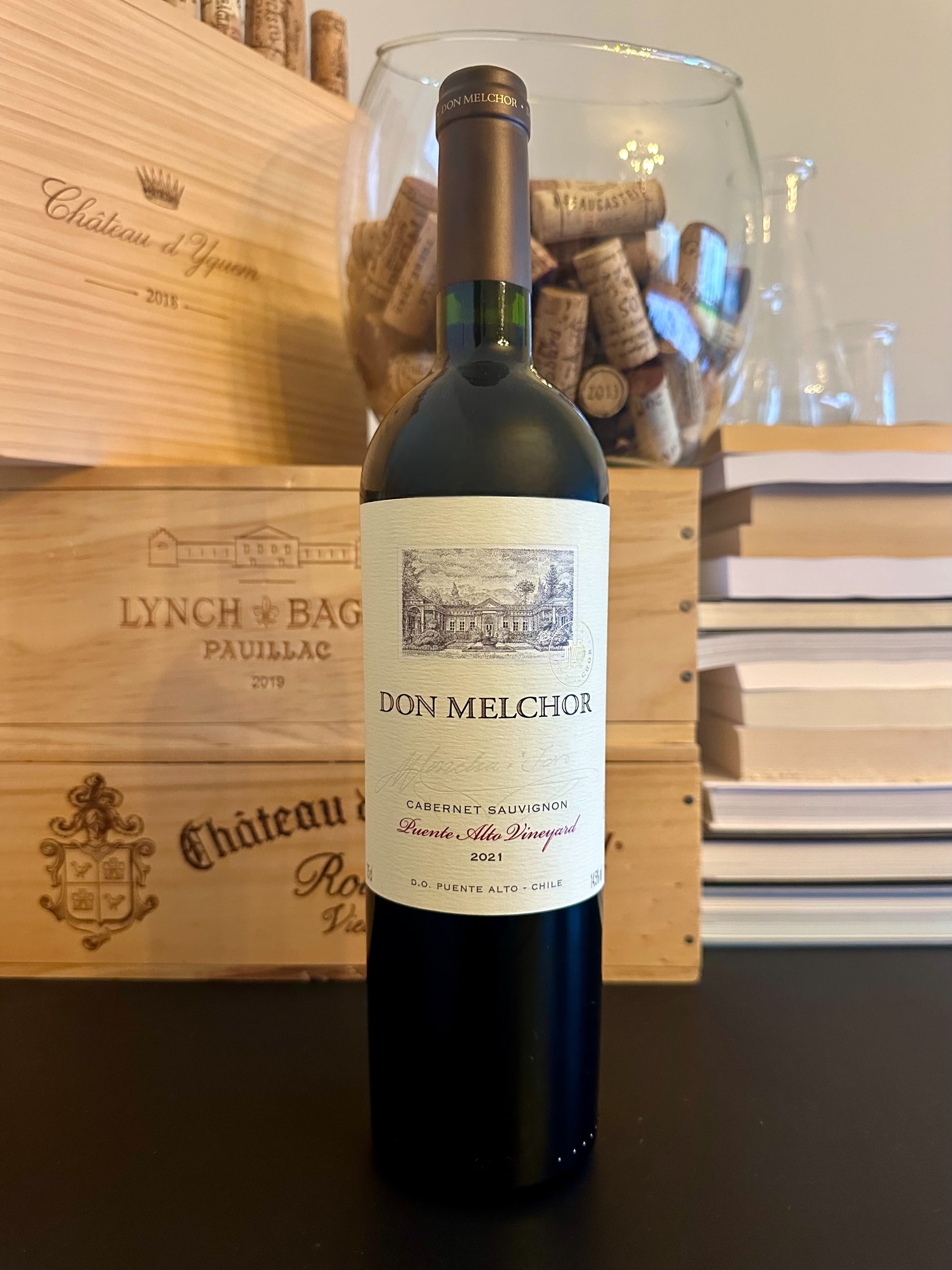 Bottle of Viña Don Melchor Cabernet Sauvignon Puente Alto Puente Alto Vineyard 2021 wine with a wooden box and corks in the background.