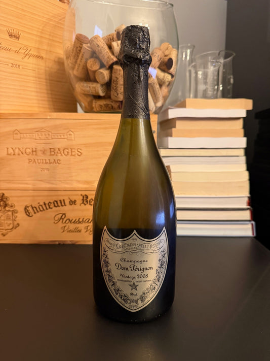 Bottle of Dom Pérignon Chef de Cave Legacy Edition 2008 with a wooden box and books in the background.