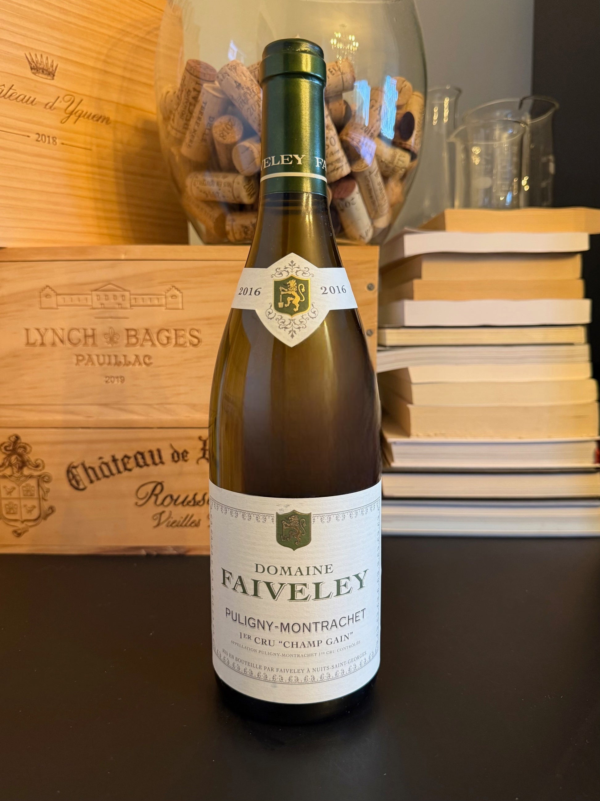 Domaine Faiveley Puligny-Montrachet 1er Cru "Champ Gain" 2016 wine bottle with a wooden box and books in the background.
