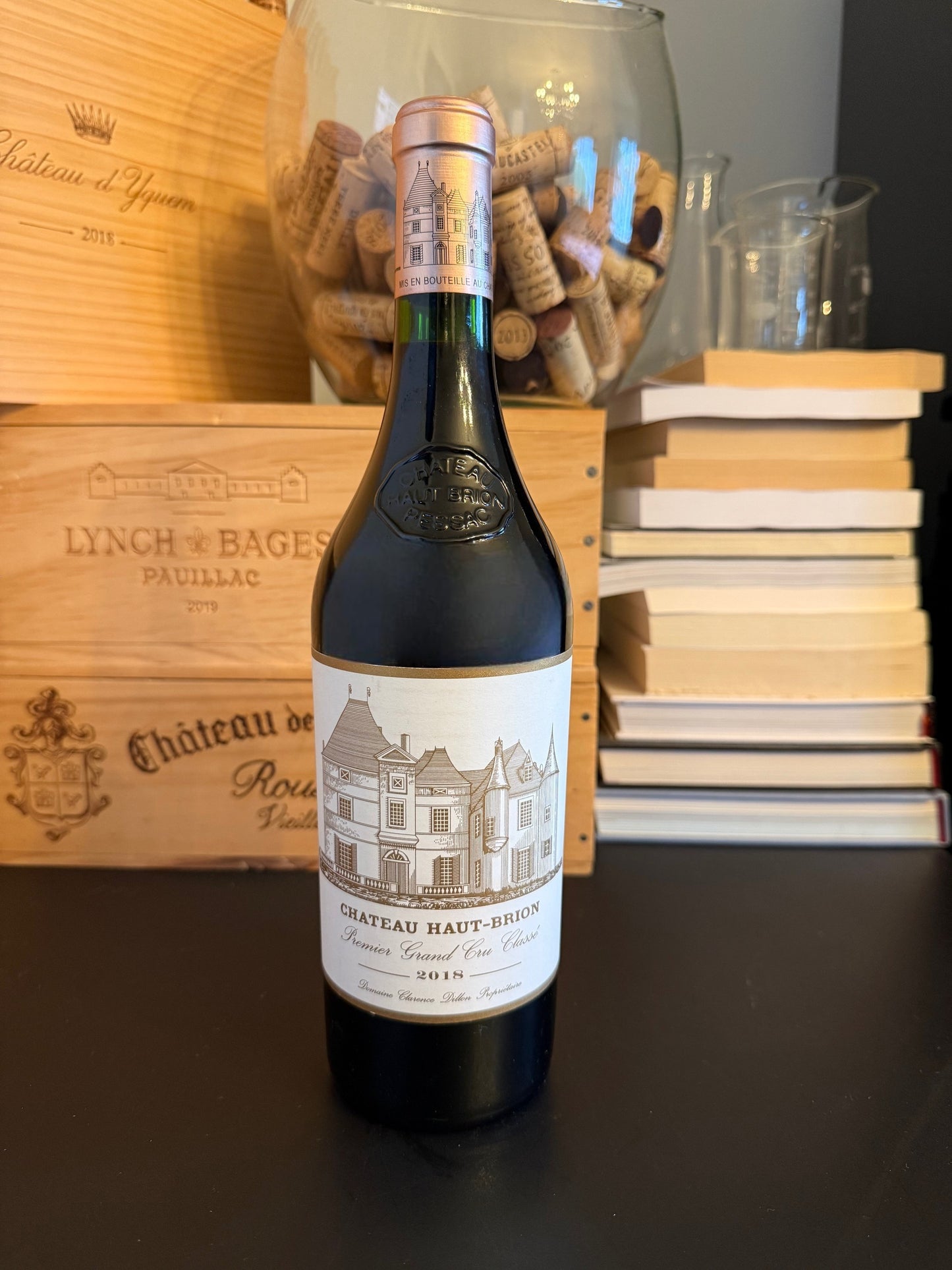 Bottle of Château Haut-Brion 2018 wine with a wooden box and books in the background.