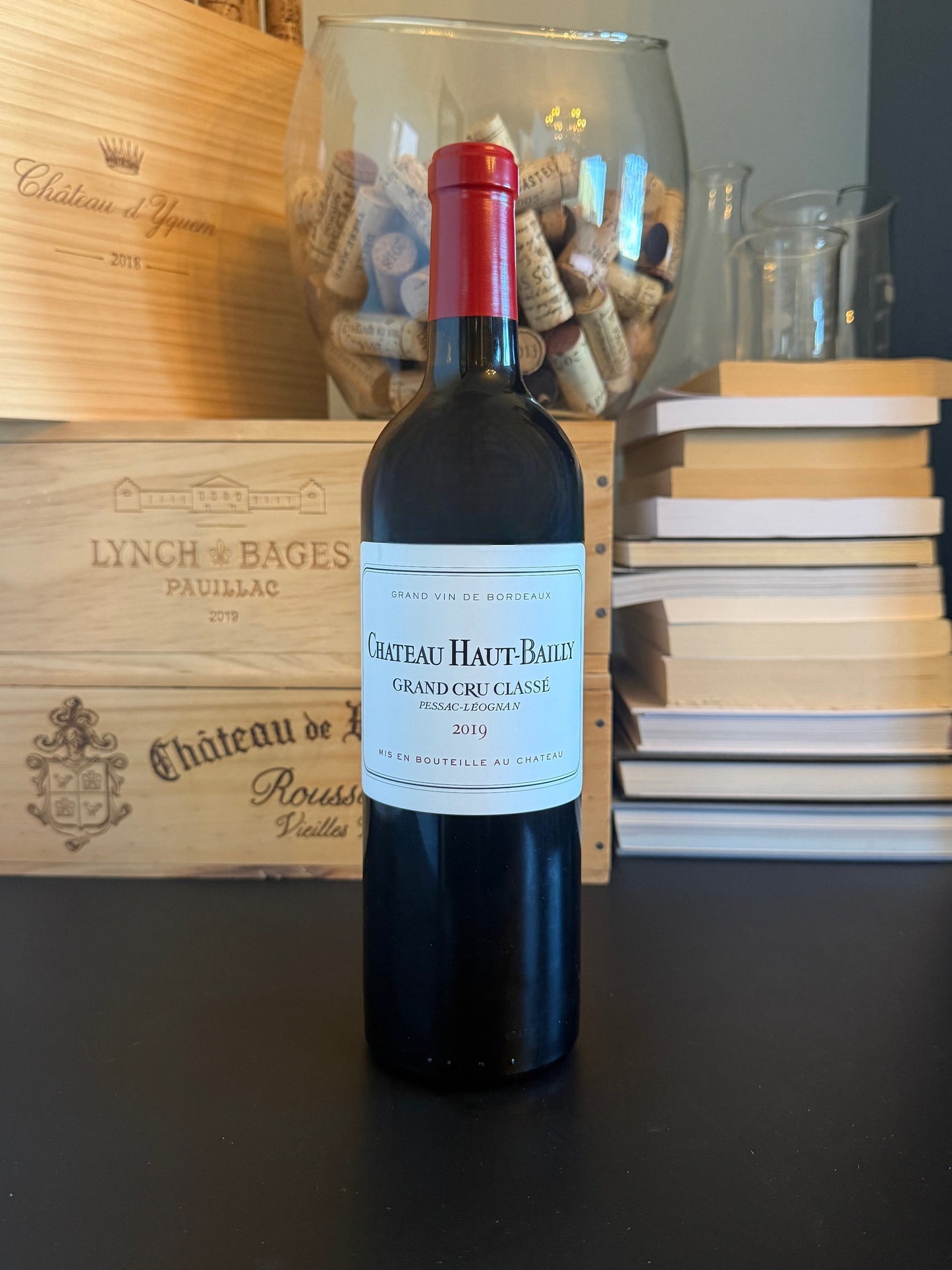 Bottle of Château Haut-Bailly 2019 wine with a wooden box and cork display in the background.