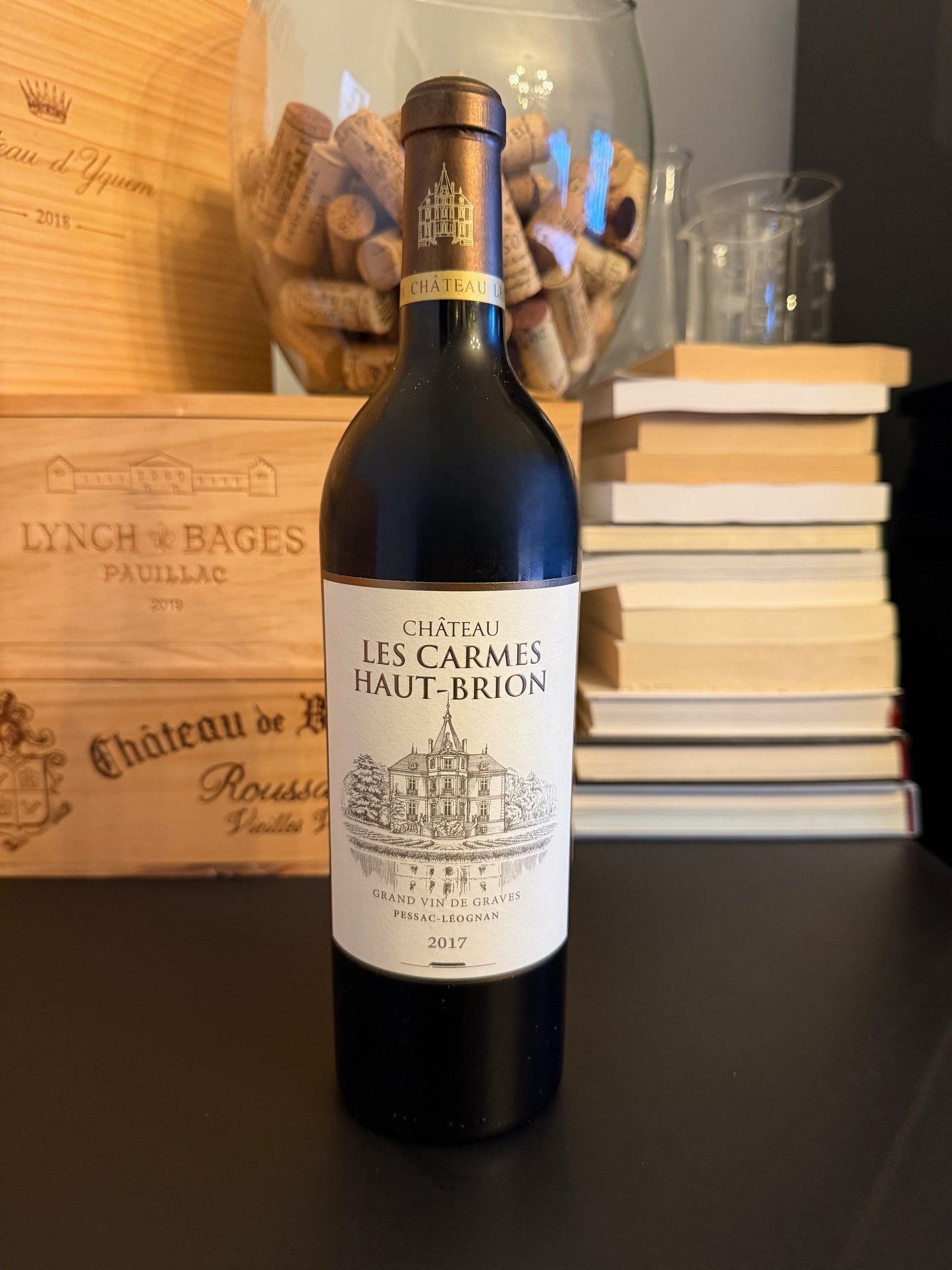 Bottle of Château Les Carmes Haut-Brion 2017 wine with a wooden box and books in the background.