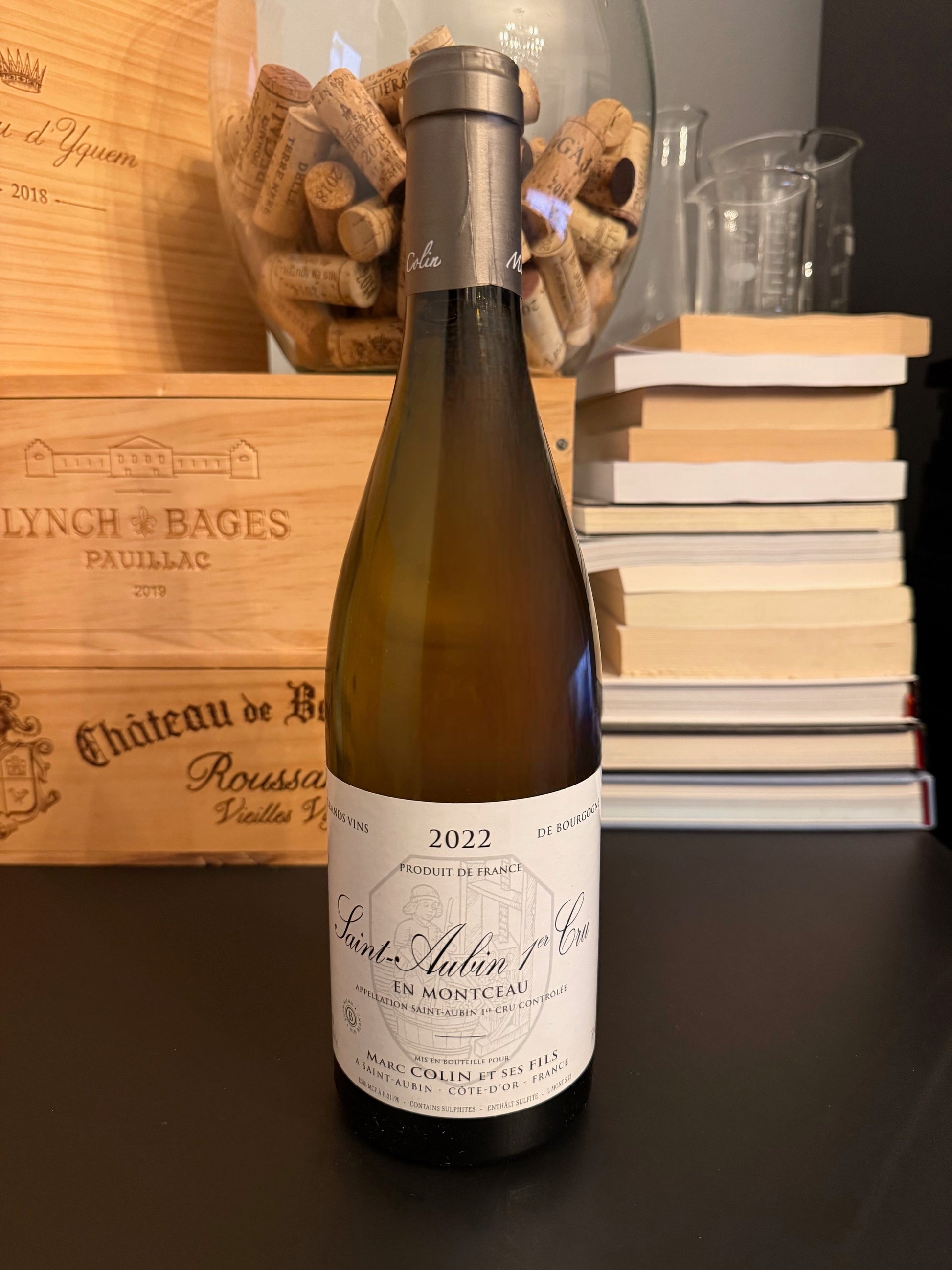 Wine bottle of Domaine Marc Colin et ses Fils Saint-Aubin 1er Cru En Montceau 2022 with a wooden box and books in the background.