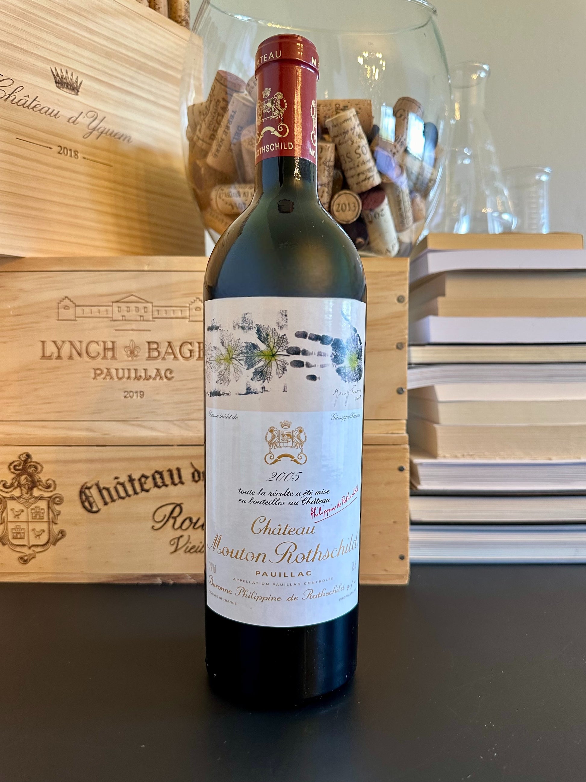 Bottle of Château Mouton Rothschild 2005 wine with a wooden box and books in the background.