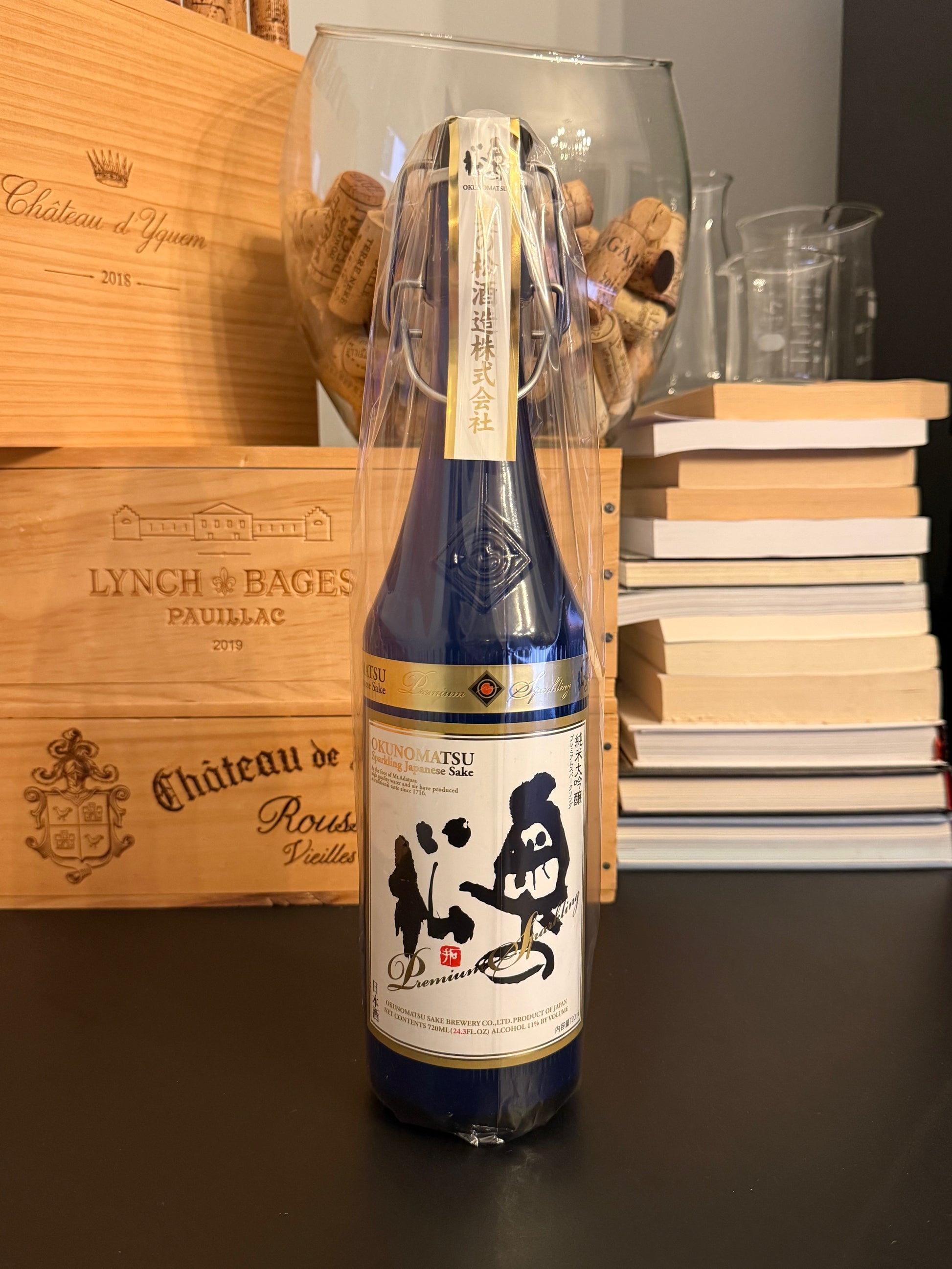 Bottle of Japanese sake Okunomatsu Sparkling on a wooden surface with books in the background.