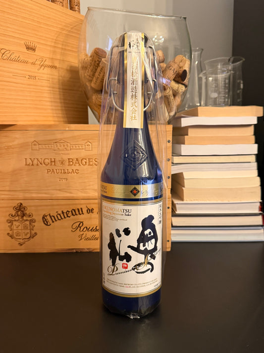 Bottle of Japanese sake Okunomatsu Sparkling on a wooden surface with books in the background.