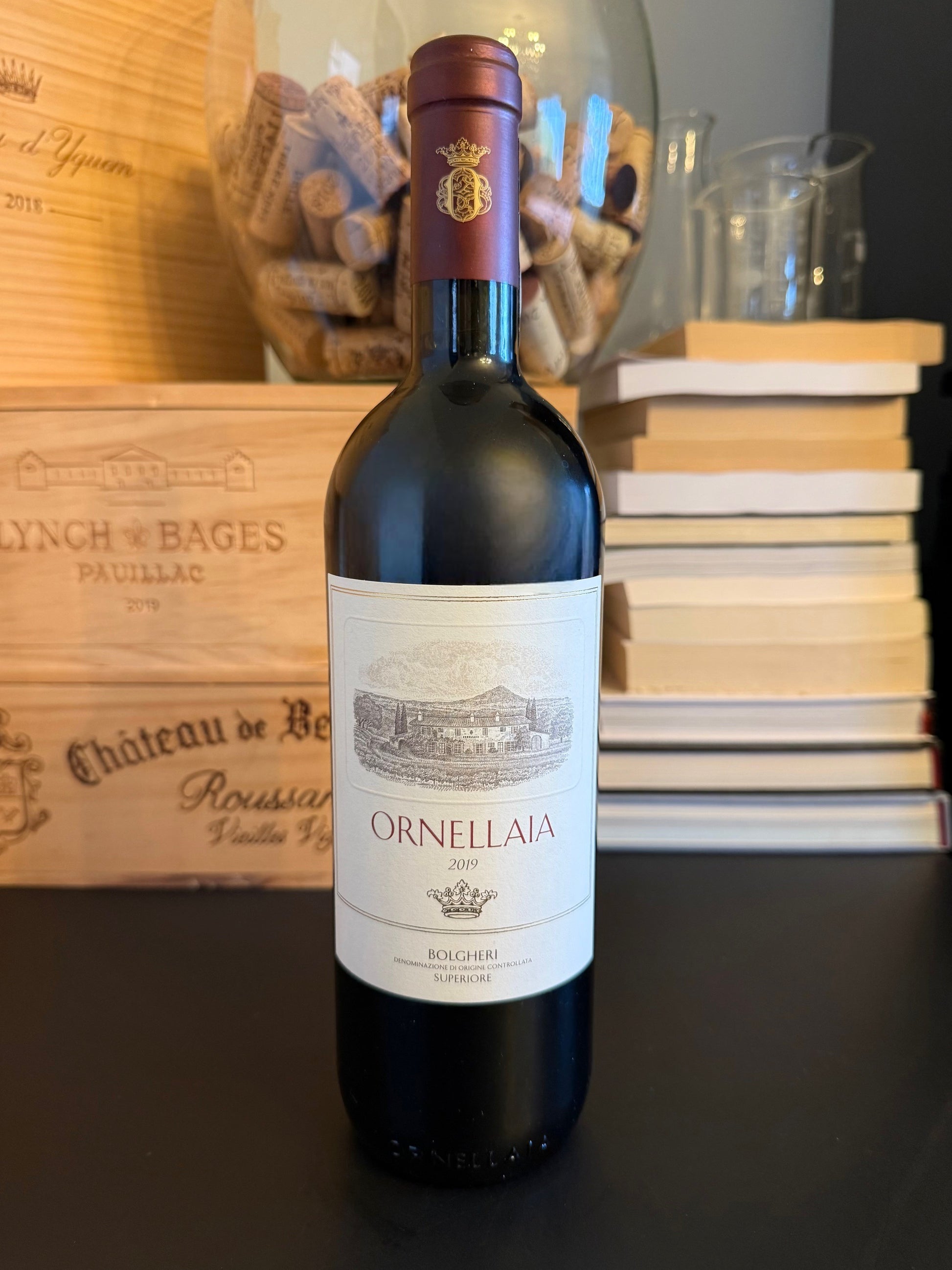 Bottle of Ornellaia Bolgheri Superiore 2019 with a wooden crate and books in the background.