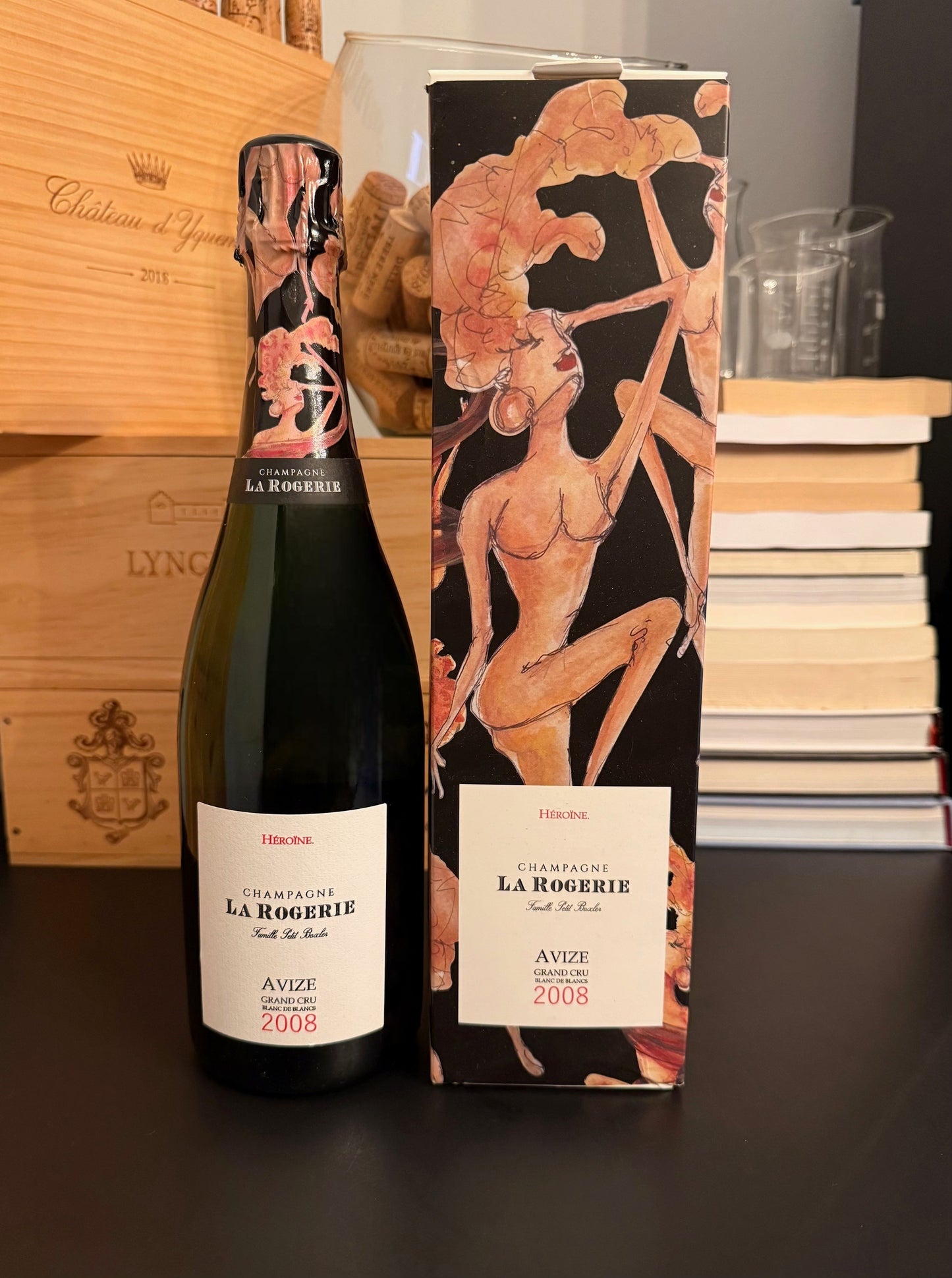 Wine bottle of La Rogerie 'Heroine' Blanc de Blancs Grand Cru Extra Brut Millesime 2008 Champagne and gift packaging with artistic design on a dark surface.
