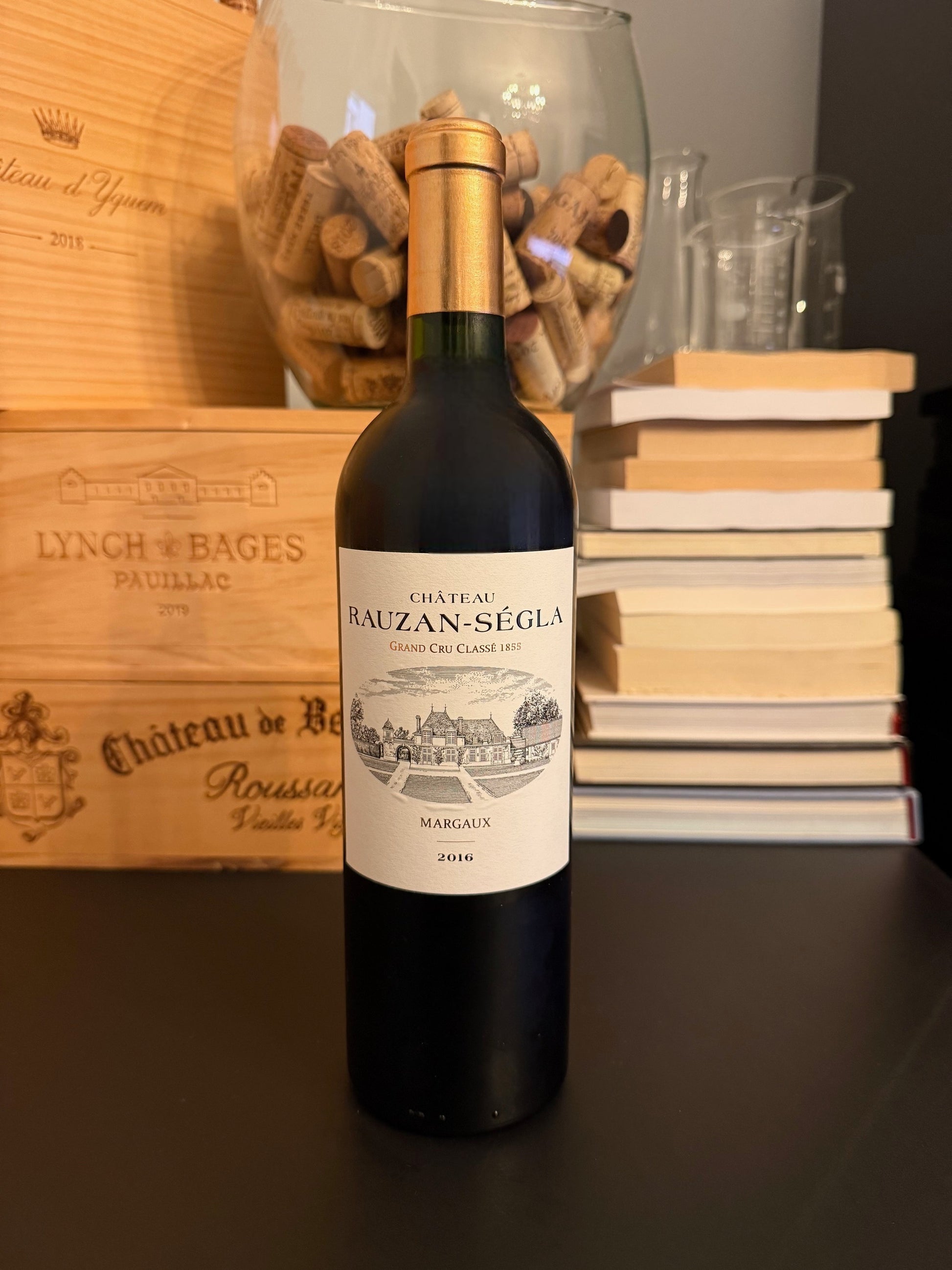 Bottle of Château Rauzan-Ségla 2016 wine with a cork display and books in the background.