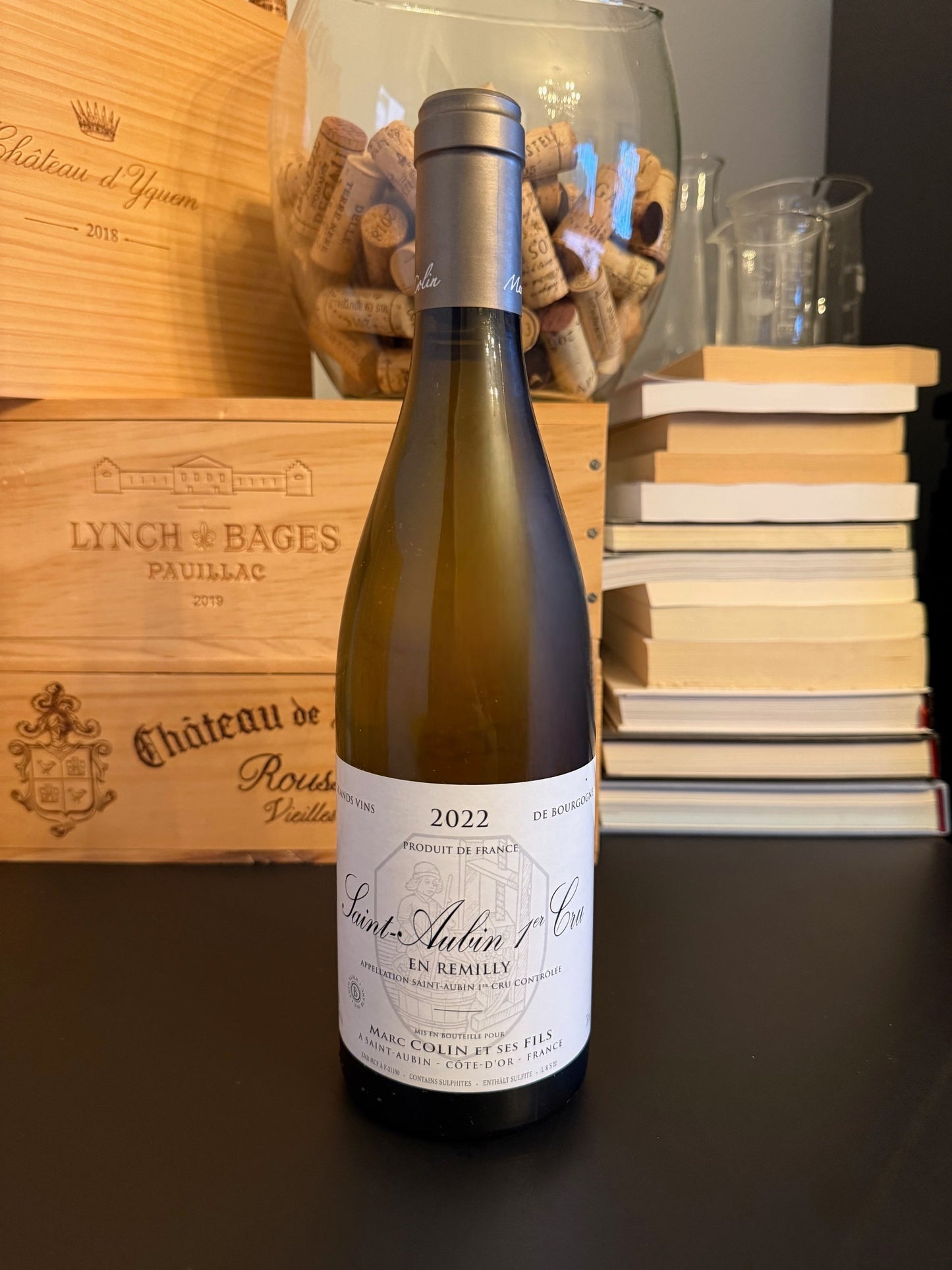 Wine bottle of Marc Colin Saint Aubin Premier Cru En Remily	2022 with a wooden box and books in the background.