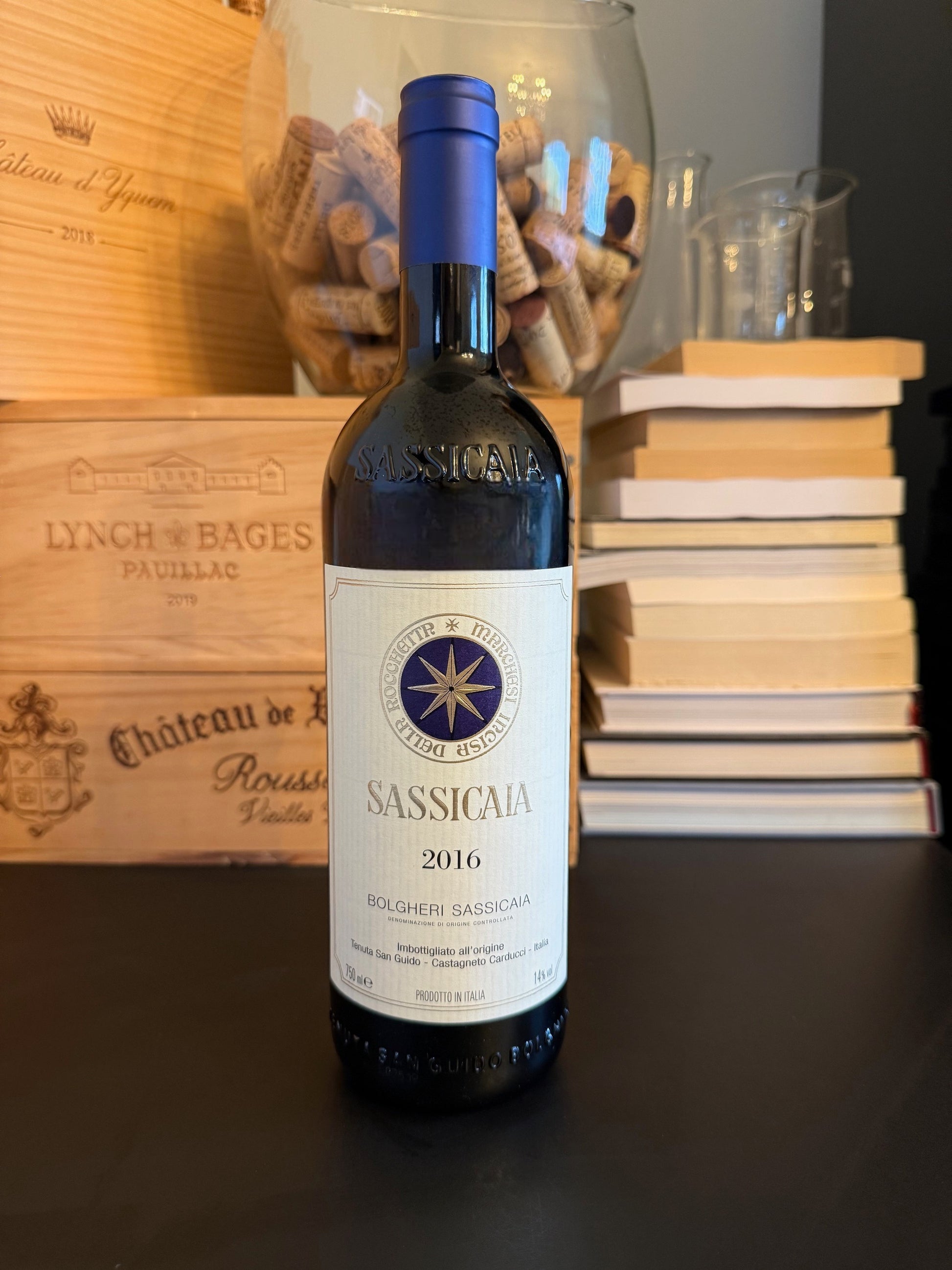 Bottle of Sassicaia 2016 wine with a wooden box and books in the background.