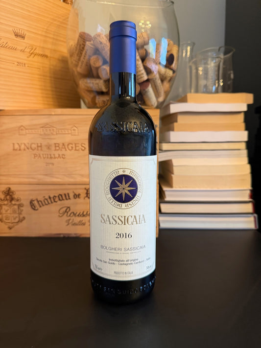 Bottle of Sassicaia 2016 wine with a wooden box and books in the background.
