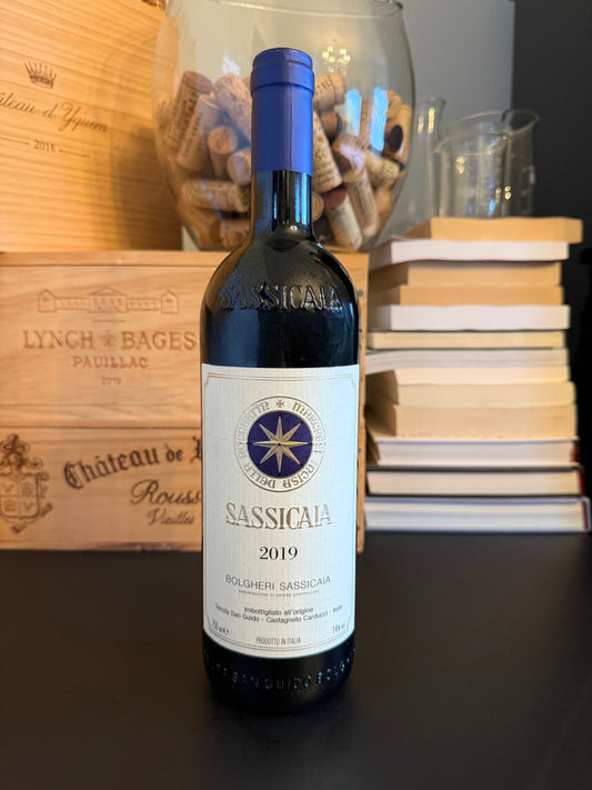 Bottle of Sassicaia 2019 wine with a wooden box and books in the background.