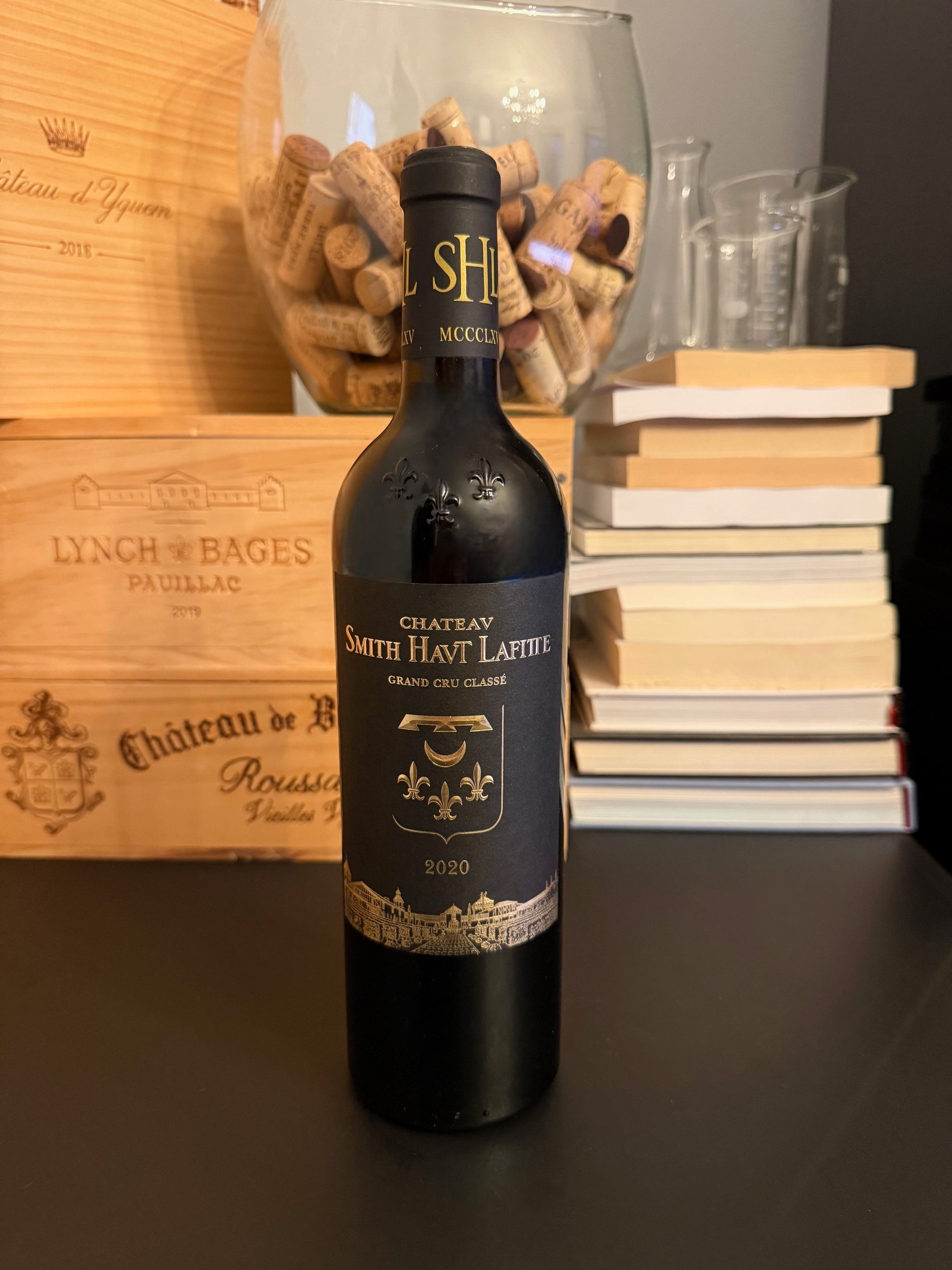 Bottle of Château Smith Haut Lafitte 2020 wine with a wooden box and books in the background.