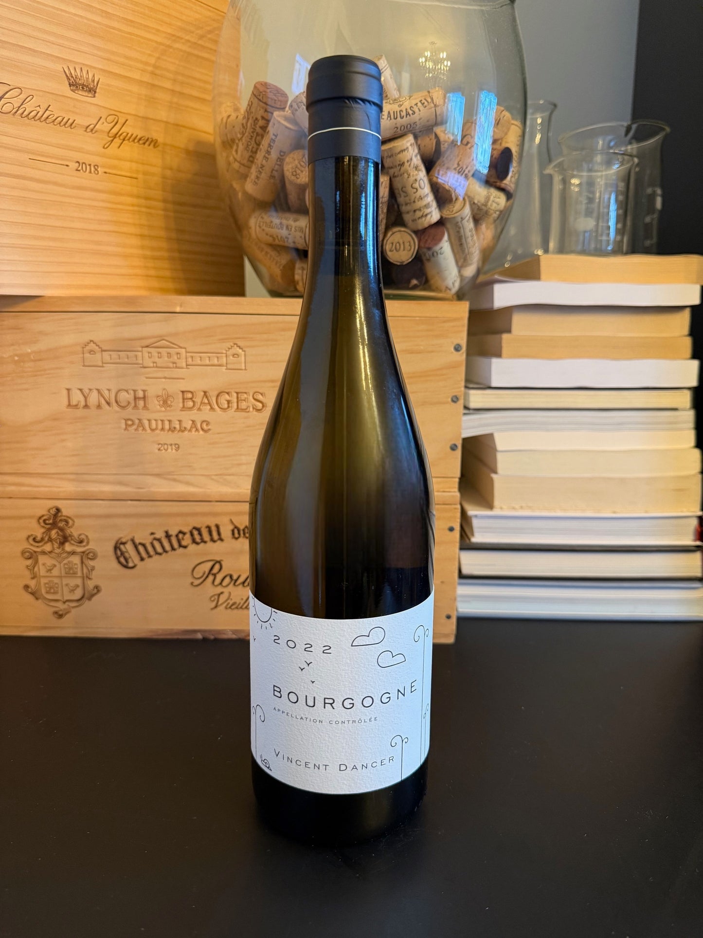 Bottle of Vincent Dancer Bourgogne Blanc 2022 wine with a wooden box and books in the background.
