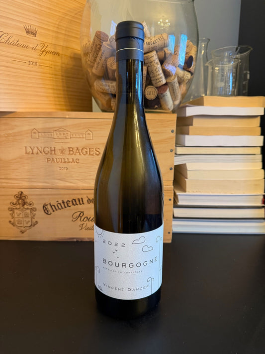 Bottle of Vincent Dancer Bourgogne Blanc 2022 wine with a wooden box and books in the background.